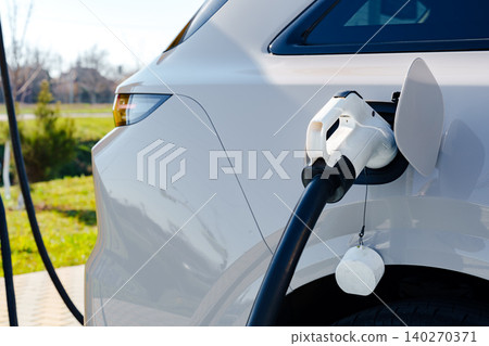 Electric car charger connected to vehicle at charging station in sunny outdoor area Electric car charger connected to vehicle at charging station in sunny outdoor area 140270371