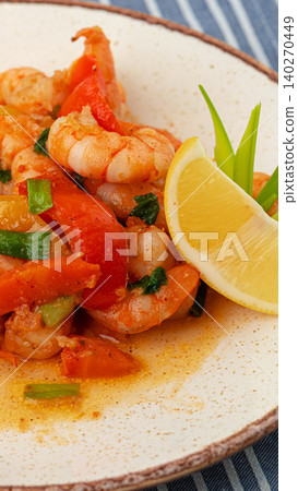 Shrimp cooked with peppers served on a plate with lemon and greens 140270449