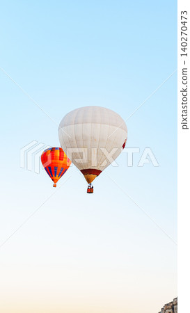 Hot air balloons rise into the clear sky over the countryside at dawn near a small town 140270473