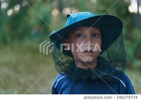 A young boy wearing a wide-brimmed anti-mosquito hat against a lush natural backdrop.Camping concept 140270734