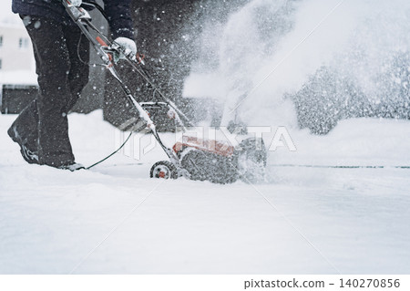 unrecognizable man clearing snow near wooden house in countryside using electric snow blower 140270856