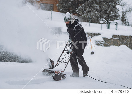 man clearing snowdrifts in countryside using electric snow blower on snowy winter day man clearing snowdrifts in countryside using electric snow blower on snowy winter day 140270860