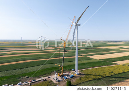 Wind turbine installation using a large construction crane. The assembly process of the turbine tower and rotor blades. Aerial view. Wind turbine installation using a large construction crane. The assembly process of the turbine tower and rotor blades. Aerial view. 140271143