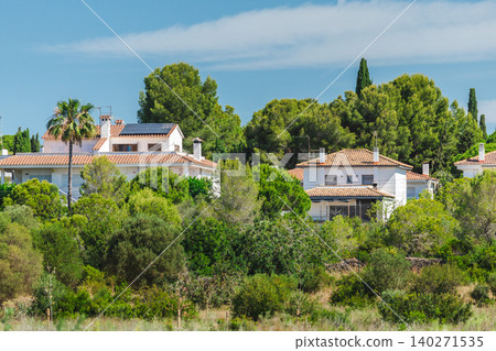 Residential neighborhood in Spain surrounded by Mediterranean vegetation and pine trees. Detached houses with tiled roofs and solar panels Residential neighborhood in Spain surrounded by Mediterranean vegetation and pine trees. Detached houses with tiled roofs and solar panels 140271535