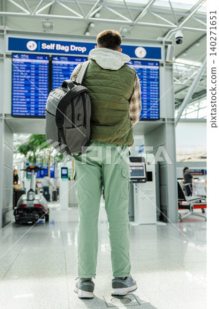 Male traveler with backpack standing in airport terminal near self bag drop and departure screens Male traveler with backpack standing in airport terminal near self bag drop and departure screens 140271651