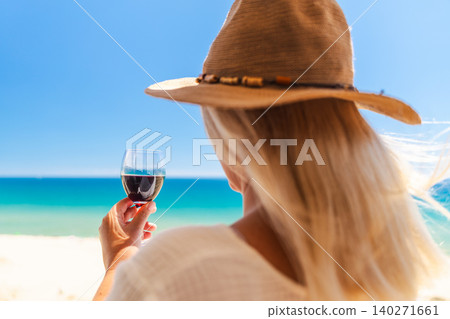 Woman relaxing with glass of red wine and turquoise sea view during sunny beach vacation in summer resort Woman relaxing with glass of red wine and turquoise sea view during sunny beach vacation in summer resort 140271661