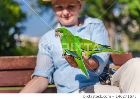 Closeup of green monk parakeets sitting on woman hand in sunny Barcelona park, colorful tropical urban birds interacting with tourist outdoors 140271675