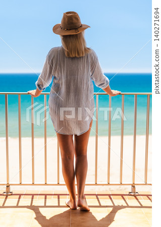 Woman in sun hat standing barefoot on balcony with turquoise sea view, summer vacation and peaceful seaside relaxation lifestyle concept Woman in sun hat standing barefoot on balcony with turquoise sea view, summer vacation and peaceful seaside relaxation lifestyle concept 140271694