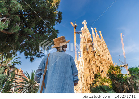 Woman traveler looking at Sagrada Familia cathedral under dramatic morning sky in Barcelona Woman traveler looking at Sagrada Familia cathedral under dramatic morning sky in Barcelona 140271711