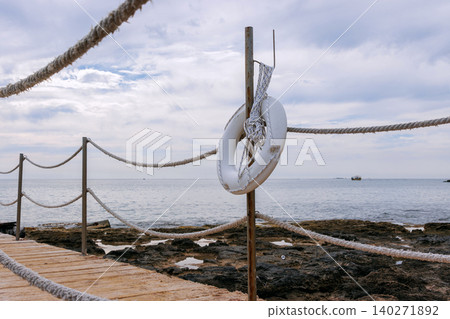 Rope fence walkway with a white lifebuoy by Mediterranean Sea in Paphos, Cyprus. Rope fence walkway with a white lifebuoy by Mediterranean Sea in Paphos, Cyprus. 140271892