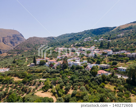 A picturesque Greek village with whitewashed houses nestled on a hill slope, overlooking a stunning mountain gorge in Crete, Greece. A perfect blend of traditional architecture and natural scenery A picturesque Greek village with whitewashed houses nestled on a hill slope, overlooking a stunning mountain gorge in Crete, Greece. A perfect blend of traditional architecture and natural scenery 140272608
