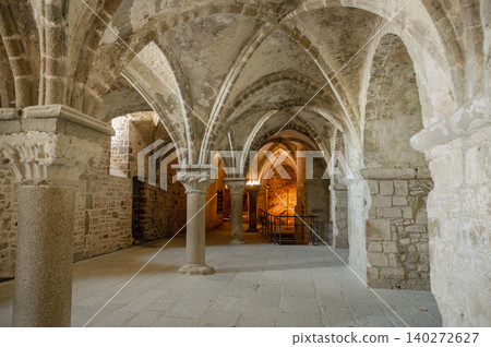 Serene and historic interior of Mont Saint-Michel Abbey with stone arches, ancient walls, and soft natural light filtering through narrow windows. Serene and historic interior of Mont Saint-Michel Abbey with stone arches, ancient walls, and soft natural light filtering through narrow windows. 140272627