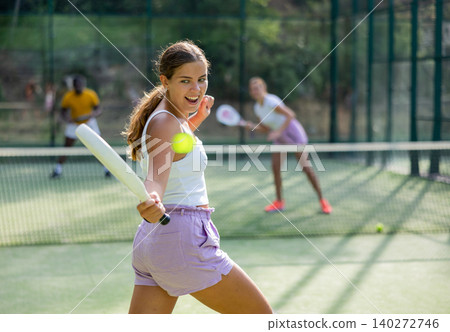 Rear view of woman playing paddle tennis match on outdoor court on blurred background of opponents 140272746