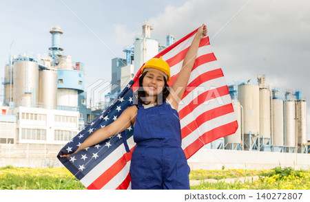 Portrait of positive girl in construction overalls with the USA flag on the background of modern factory Portrait of positive girl in construction overalls with the USA flag on the background of modern factory 140272807