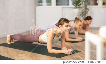 Diligent women practicing plank pose of yoga in light fitness room Diligent women practicing plank pose of yoga in light fitness room 140272840