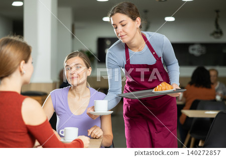 Girl waiter in apron presents coffee and croissants to restaurants guests Girl waiter in apron presents coffee and croissants to restaurants guests 140272857