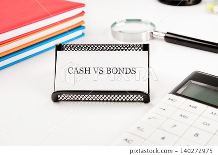 On a clean desk, a sign reading cash vs bonds stands out next to a calculator, magnifying glass, and colorful notebooks, suggesting focused financial analysis On a clean desk, a sign reading cash vs bonds stands out next to a calculator, magnifying glass, and colorful notebooks, suggesting focused financial analysis 140272975