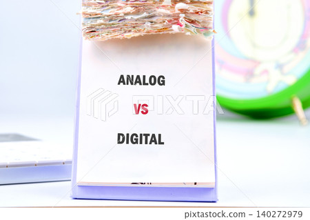 A colorful workspace showcases a card displaying Analog vs Digital alongside an old-fashioned clock, emphasizing the clash between traditional and modern methods of timekeeping A colorful workspace showcases a card displaying Analog vs Digital alongside an old-fashioned clock, emphasizing the clash between traditional and modern methods of timekeeping 140272979