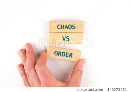 A hand reaches for wooden blocks displaying the words chaos and order, symbolizing a playful exploration of contrasting concepts in a thoughtful activity 140272981