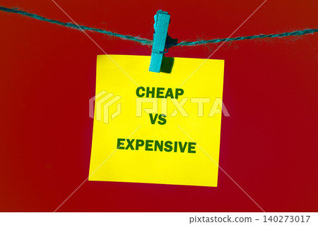 A yellow sticky note hangs against a bold red backdrop, displaying the words cheap and expensive. This visual sparks thoughts about value and budgeting A yellow sticky note hangs against a bold red backdrop, displaying the words cheap and expensive. This visual sparks thoughts about value and budgeting 140273017
