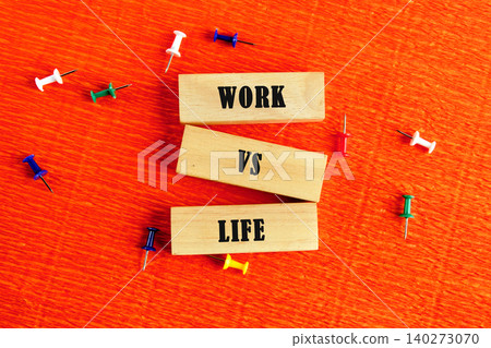 Two wooden blocks are arranged on a vibrant orange surface, boldly showcasing the words work and life. Colorful push pins surround them, illustrating a creative contrast Two wooden blocks are arranged on a vibrant orange surface, boldly showcasing the words work and life. Colorful push pins surround them, illustrating a creative contrast 140273070