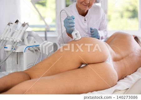 Aesthetician administering ice hammer therapy to tighten skin on female buttocks Aesthetician administering ice hammer therapy to tighten skin on female buttocks 140273086