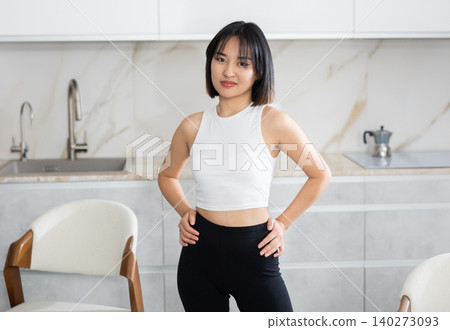 Smiling young Asian girl standing at table in the kitchen Smiling young Asian girl standing at table in the kitchen 140273093