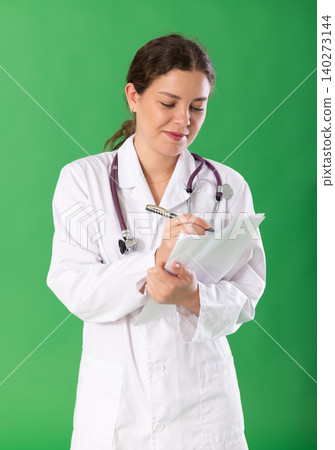 Young woman doctor in white coat with a stethoscope conducts a survey remotely green background Young woman doctor in white coat with a stethoscope conducts a survey remotely green background 140273144