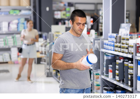 Interested young handyman choosing paints in construction hypermarket Interested young handyman choosing paints in construction hypermarket 140273317