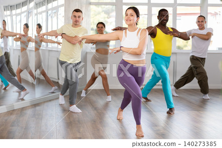 Smiling woman with multinational group active people enthusiastically training social latin cha-cha-cha dance movements in dance salon Smiling woman with multinational group active people enthusiastically training social latin cha-cha-cha dance movements in dance salon 140273385