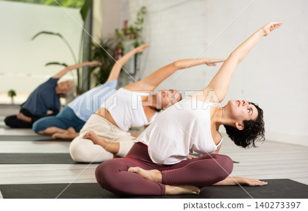 Young Latin woman performing arm bends sitting in Lotus pose, warming up before practicing asanas in yoga studio Young Latin woman performing arm bends sitting in Lotus pose, warming up before practicing asanas in yoga studio 140273397