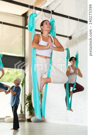 Yogi woman doing fly yoga stretching exercises on hammock in gym. Adult female coach helps girl in stretch on background 140273399