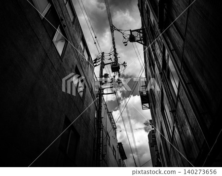 A cloudy sky viewed from between buildings; a monochrome cityscape. A cloudy sky viewed from between buildings; a monochrome cityscape. 140273656