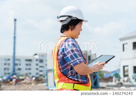 Construction engineer using digital tablet at building site wearing safety equipment monitoring project progress an active construction environment 140274243