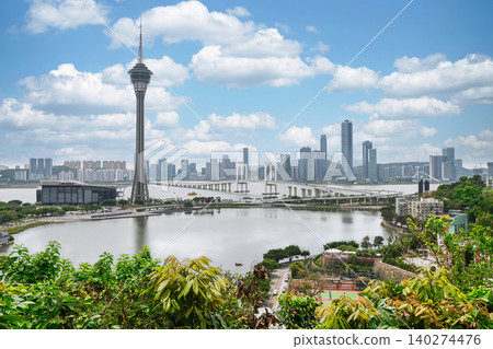 Panoramic view of Macau Tower and Sai Van Bridge across water with modern city skyline under blue sky with white cloud Panoramic view of Macau Tower and Sai Van Bridge across water with modern city skyline under blue sky with white cloud 140274476