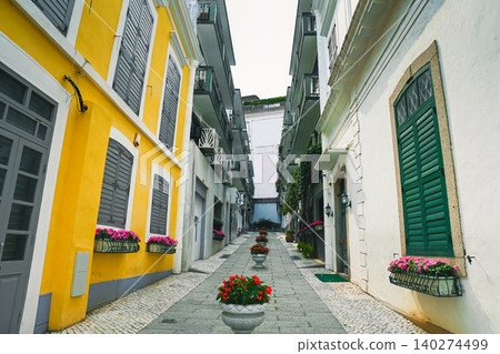 Traditional cobblestone alley with colorful yellow and white colonial buildings decorated with flower pots in mediterranean style historic street Traditional cobblestone alley with colorful yellow and white colonial buildings decorated with flower pots in mediterranean style historic street 140274499