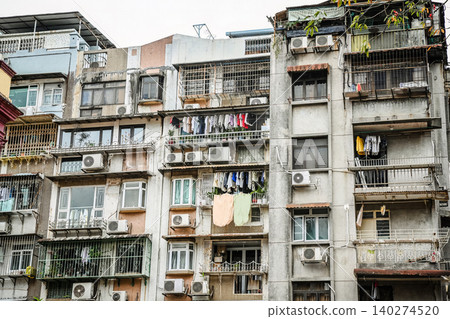 Dense residential buildings with drying laundry on balconies and air conditioners on old concrete apartment facades in Macau Dense residential buildings with drying laundry on balconies and air conditioners on old concrete apartment facades in Macau 140274520