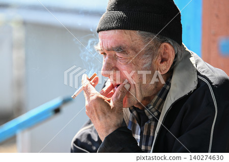 Thoughtful russian 77 years old elderly man smoking cigarette with sad face expression outdoors in poor neighborhood in russia Thoughtful russian 77 years old elderly man smoking cigarette with sad face expression outdoors in poor neighborhood in russia 140274630