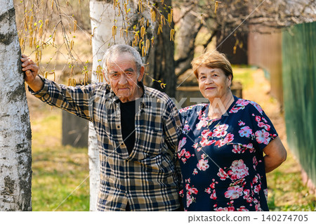 Portrait of senior russian couple husband 77 years old and wife 73 years old standing near birch tree in rural village garden Portrait of senior russian couple husband 77 years old and wife 73 years old standing near birch tree in rural village garden 140274705