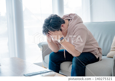 A middle-aged man holding his head in his hands in the living room. 140275321