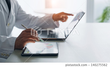 A man in a white coat working with a laptop and a tablet PC. A man in a white coat working with a laptop and a tablet PC. 140275562