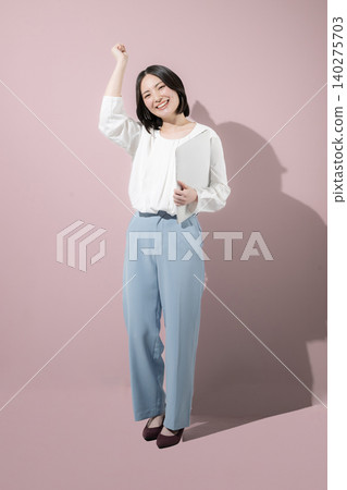 A cute, smiling female employee with a laptop against a pink background, looking directly at the camera in a full-body business image. A cute, smiling female employee with a laptop against a pink background, looking directly at the camera in a full-body business image. 140275703