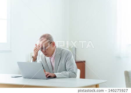 An elderly man using a computer with a troubled expression. An elderly man using a computer with a troubled expression. 140275927
