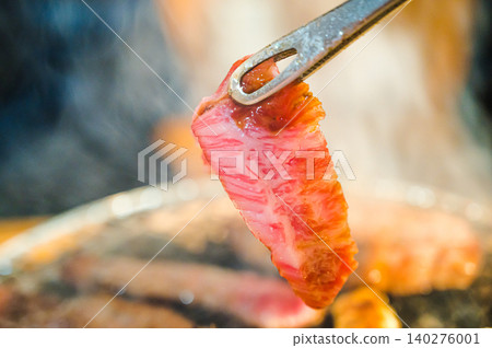 The hand holding the grilled meat with tongs The hand holding the grilled meat with tongs 140276001