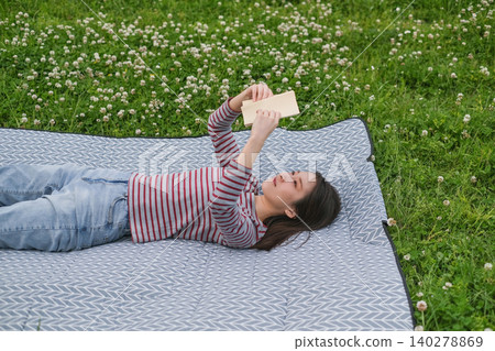 A woman lying on a picnic blanket reading a book. A woman lying on a picnic blanket reading a book. 140278869