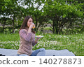 A woman eating a meal while sitting on a picnic blanket during the season of fresh greenery. 140278873