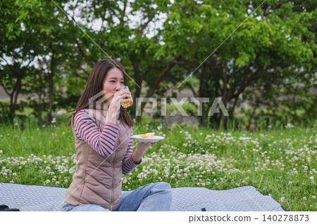 A woman eating a meal while sitting on a picnic blanket during the season of fresh greenery. A woman eating a meal while sitting on a picnic blanket during the season of fresh greenery. 140278873