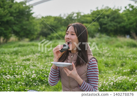 Close-up of a woman eating a rice ball at a picnic. Close-up of a woman eating a rice ball at a picnic. 140278876