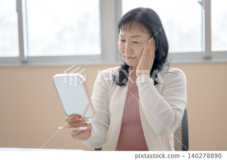 A middle-aged woman checks her skin in the mirror. A middle-aged woman checks her skin in the mirror. 140278890