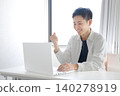 一名年輕男子在電腦前工作時，做出了一個得意的手勢。 140278919